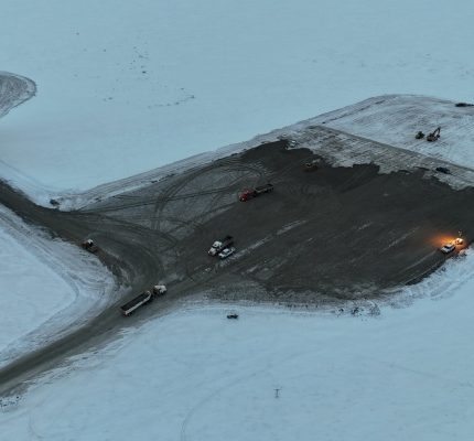 Aerial view of the project site surrounded by snow with a clearing in the middle where construction activity is taking place.