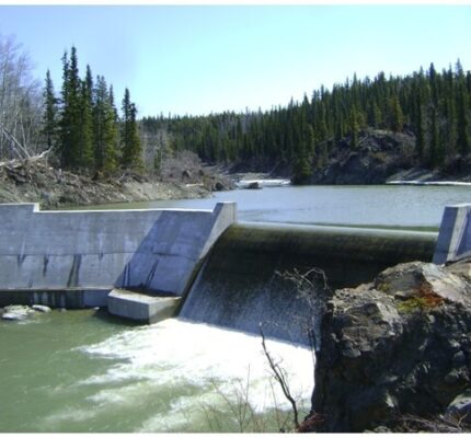 The Atlin hydroelectric dam with water running over it and trees in the background