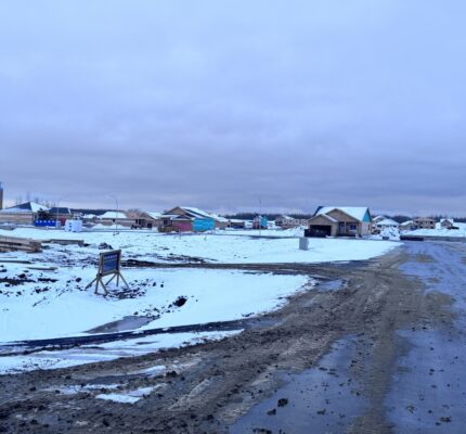 Houses being constructed with a snowy backdrop – road with snow and construction