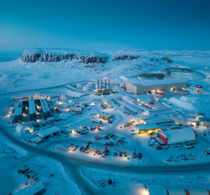 Aerial view of the Hope Bay Mine and processing site in a snow-covered Arctic landscape at dusk. Illuminated buildings, storage areas, roads and heavy equipment are spread across the site.