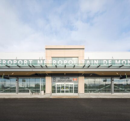 Vue frontale de l’entrée de l’aérogare pour vols intérieurs de l’aéroport métropolitain de Montréal (YHU), avec sa façade en verre, ses portes d’entrée coulissantes et le nom du bâtiment inscrit sur l’auvent extérieur supérieur.