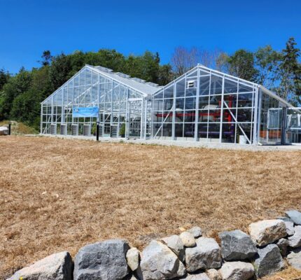 A glass‑and‑metal building at the Port Stalashen wastewater treatment facility, with trees and clear sky behind it.