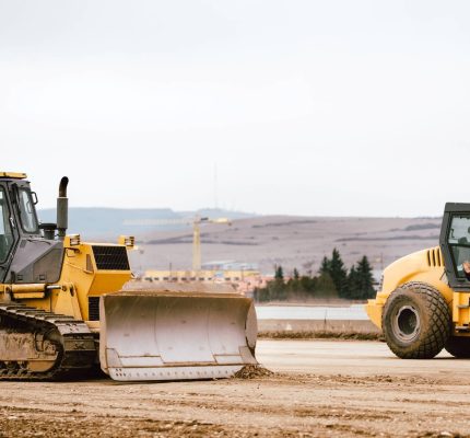 Two bulldozers on a road under construction with a construction worker motioning them to stop.