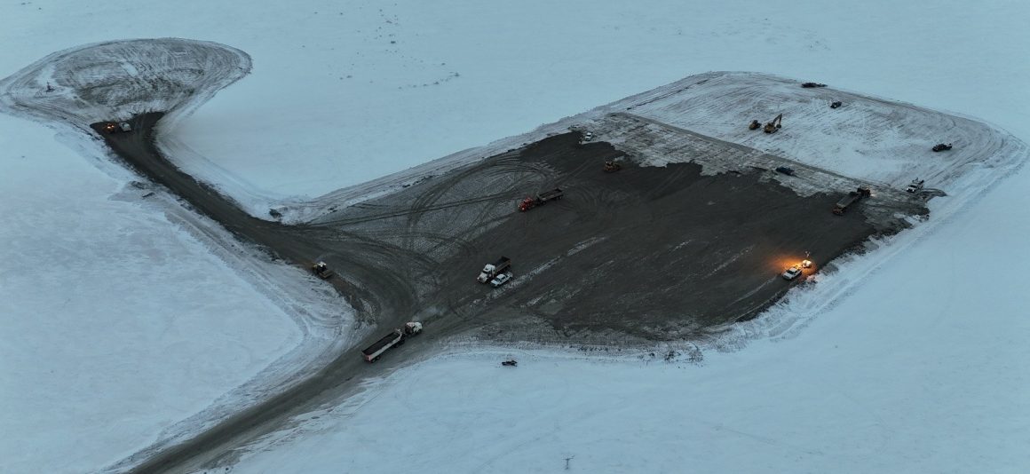 Aerial view of the project site surrounded by snow with a clearing in the middle where construction activity is taking place.