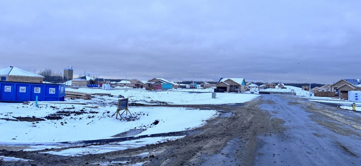 Houses being constructed with a snowy backdrop – road with snow and construction