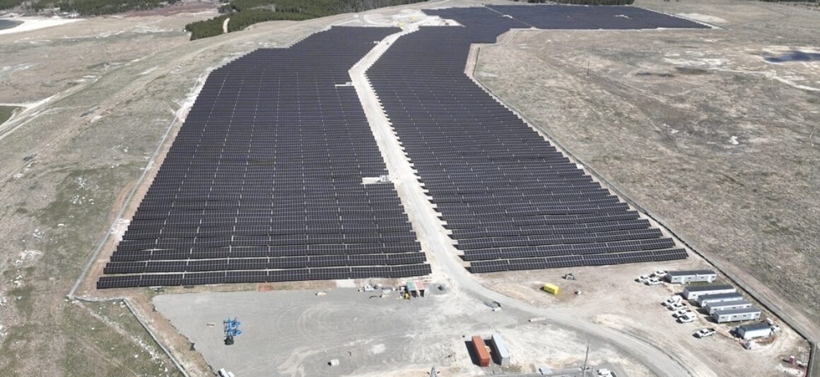 Vue aérienne de panneaux solaires dans un champ ouvert avec des montagnes au loin.
