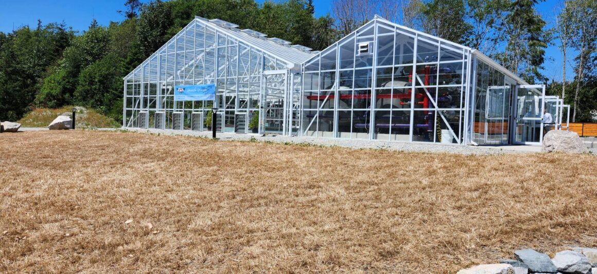 A glass‑and‑metal building at the Port Stalashen wastewater treatment facility, with trees and clear sky behind it.
