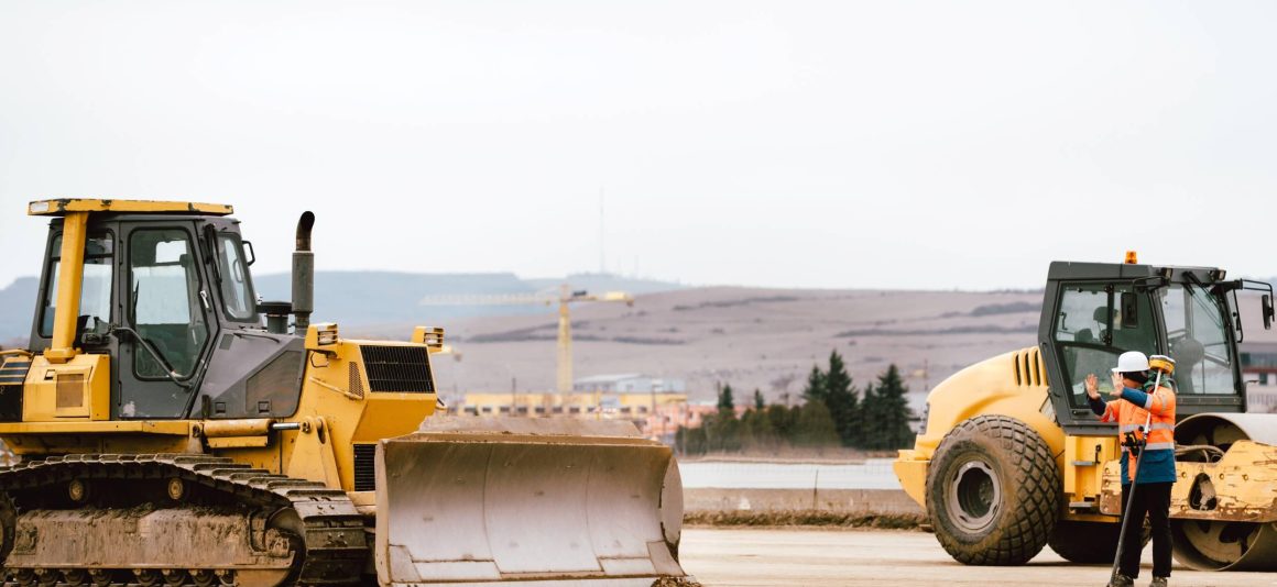 Two bulldozers on a road under construction with a construction worker motioning them to stop.