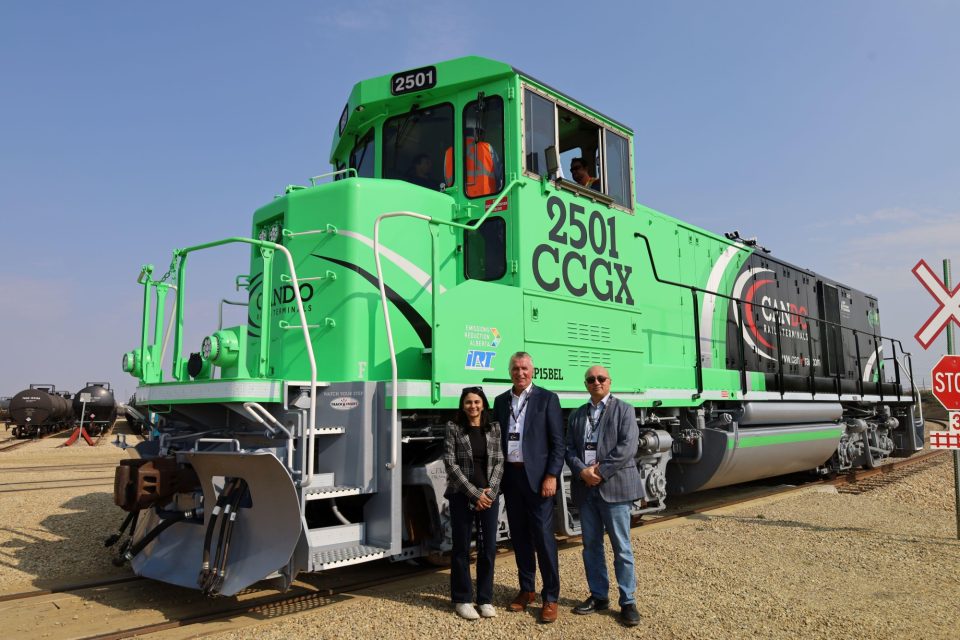 Trois personnes représentant la BIC et Cando Rail & Terminals debout devant une locomotive verte.