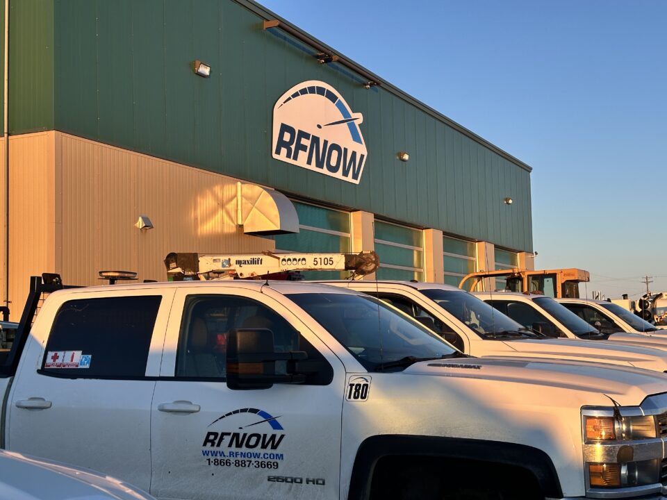 White RFNOW trucks are parked under clear blue skies at a company office.