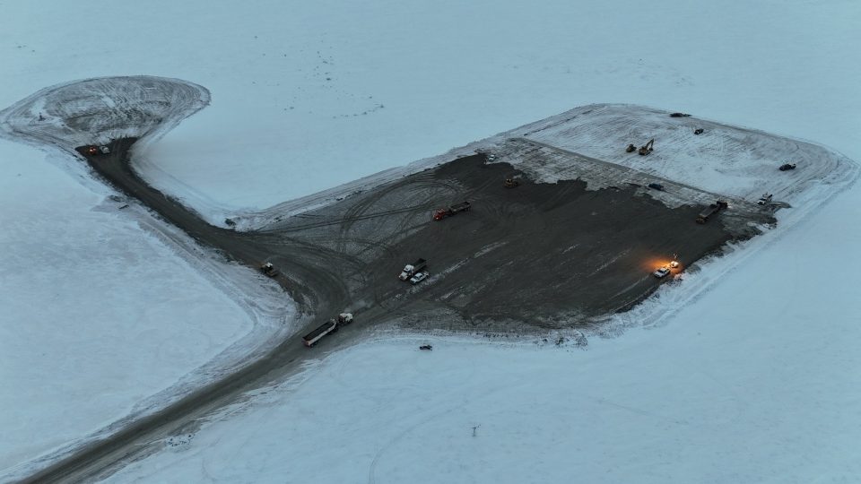 Aerial view of the project site surrounded by snow with a clearing in the middle where construction activity is taking place.