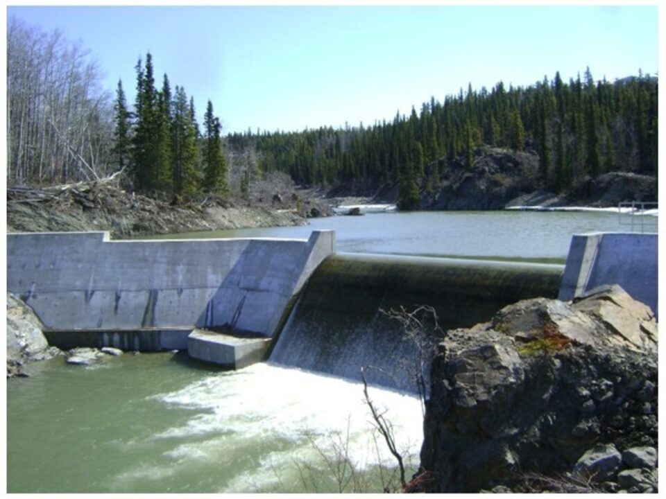 The Atlin hydroelectric dam with water running over it and trees in the background