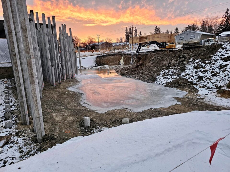 A winter scene at a construction site, showing snow and ice on the ground, along with construction equipment and materials.