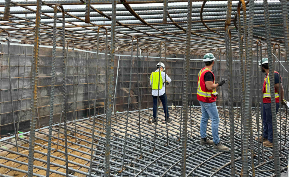 Des personnes travaillent à la fixation de barres d’armature métalliques à la base d’une plateforme d’éolienne.
