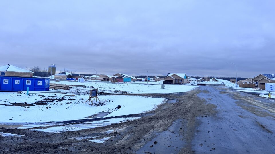 Houses being constructed with a snowy backdrop – road with snow and construction