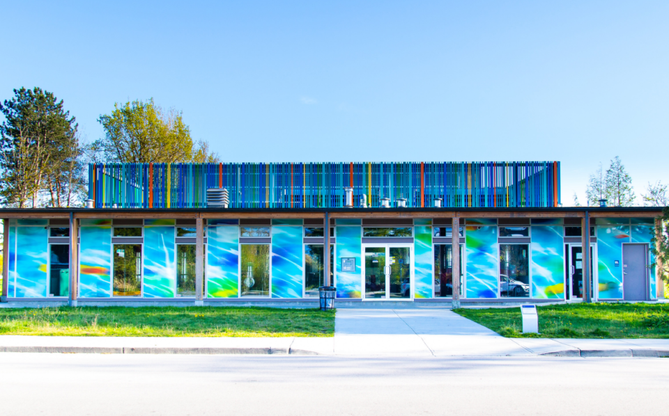 Un bâtiment d'un étage avec une rangée de fenêtres et une porte au centre; sur le toit se trouve une structure multicolore