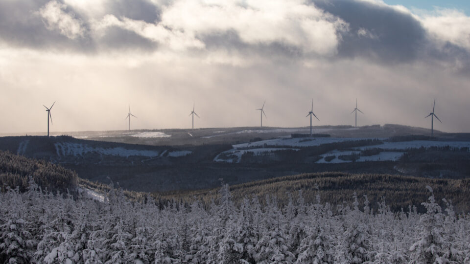 Snowy landscape with wind turbines on a hilltop under a cloudy sky.