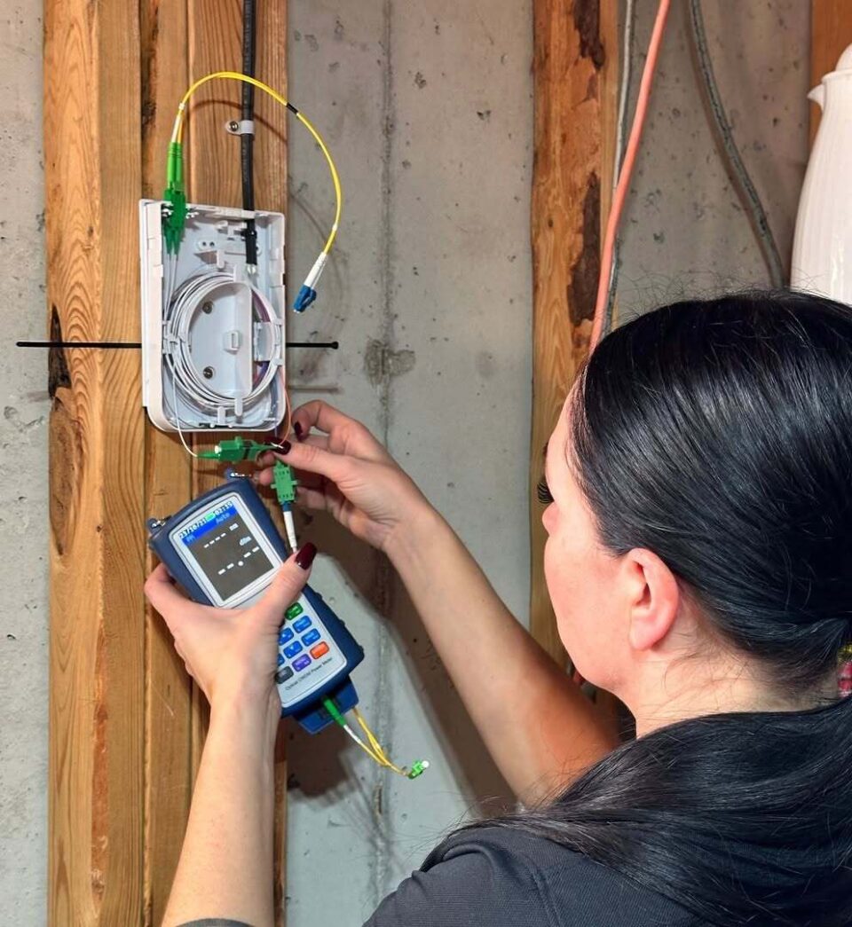 A worker uses equipment to test a fibre-optic media converter inside a property.