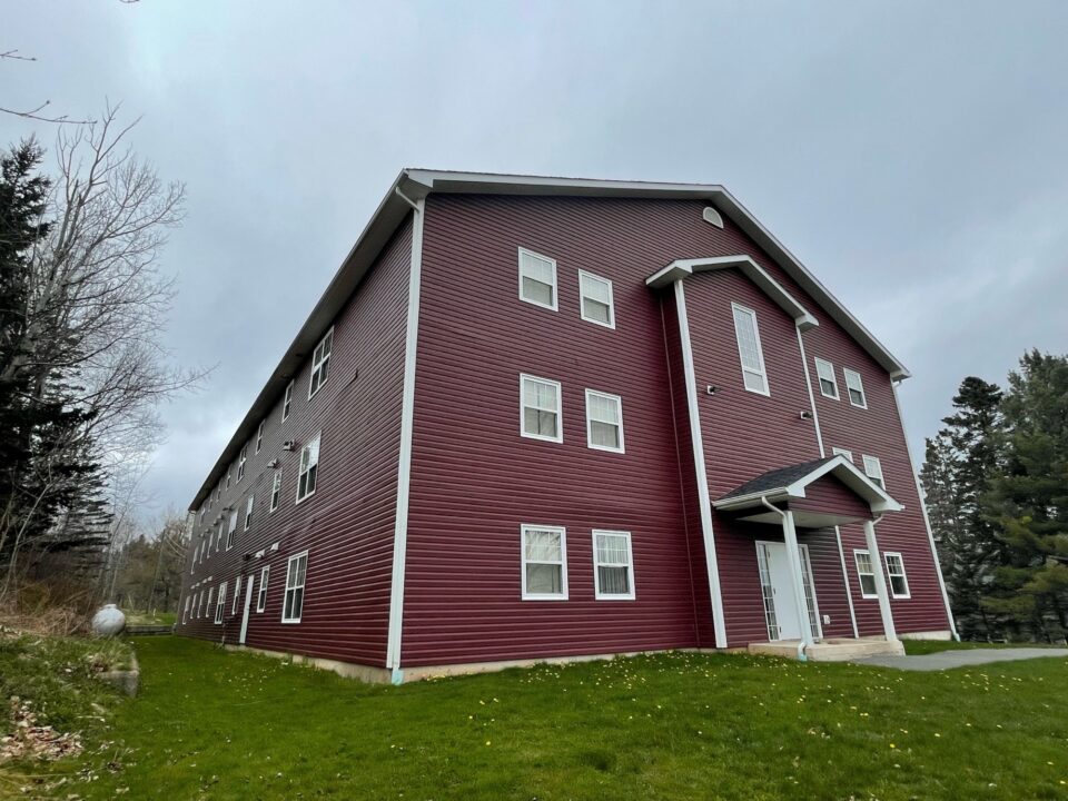 Front of red Student Housing in Sackville, New Brunswick with blue sky and green grass