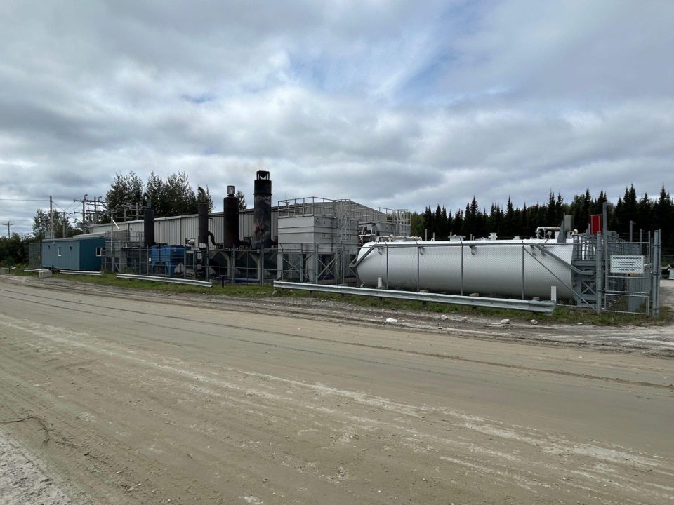 Installation de la centrale au diesel actuelle à Opitciwan qui sera remplacée par la centrale de cogénération avec un gros réservoir cylindrique et des bâtiments modulaires sous un ciel nuageux.