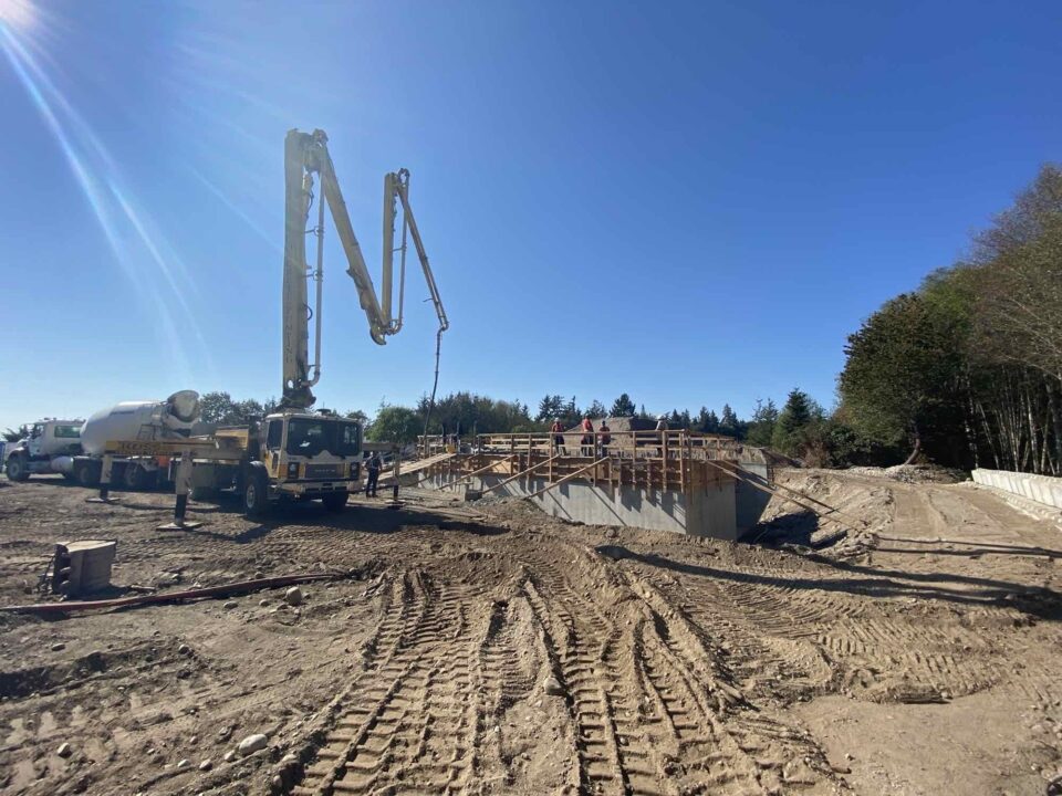 A construction site; in the foreground is a cement truck and a pump truck; several workers are on the site.