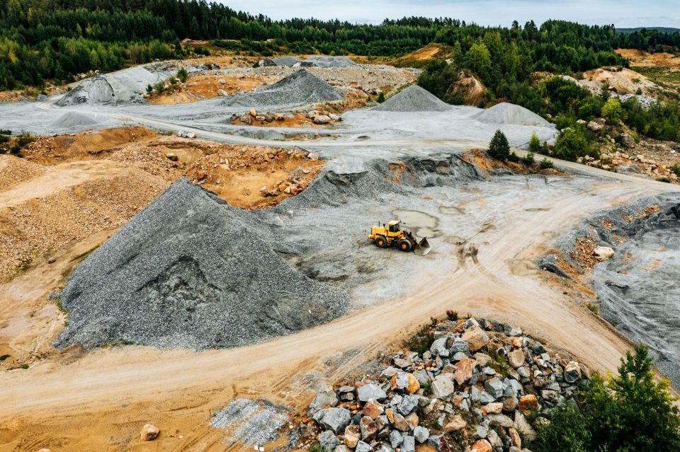 Quarry with piles of sand and a yellow excavator.