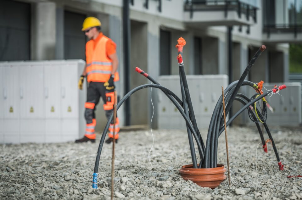 Des câbles qui sortent du sol sur un chantier de construction avec une personne travaillant à l’arrière-plan
