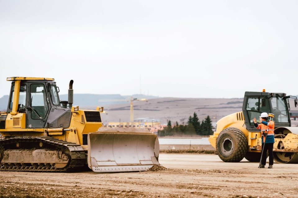 Two bulldozers on a road under construction with a construction worker motioning them to stop.