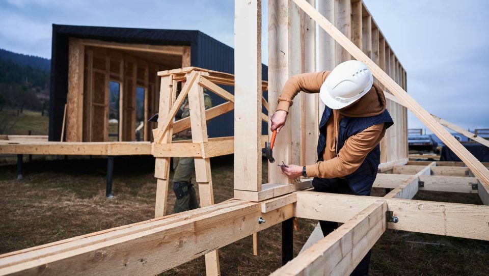 Worker hammering while building wooden frame house.