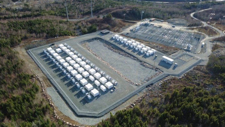 Vue aérienne du site de stockage de batteries achevé de Spider Lake, avec des rangées d’unités de stockage de batteries de la taille de conteneurs d’expédition blancs à côté d’une sous-station électrique, entourées d’une forêt dense et vert foncé.