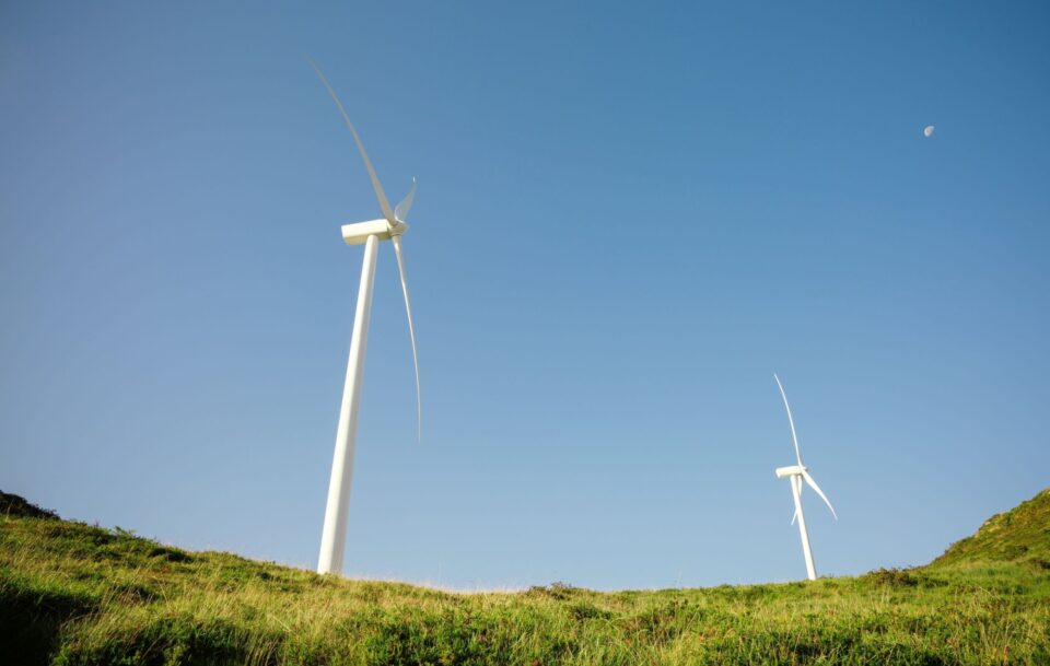 Two wind turbines on a grassy hill generating electricity.