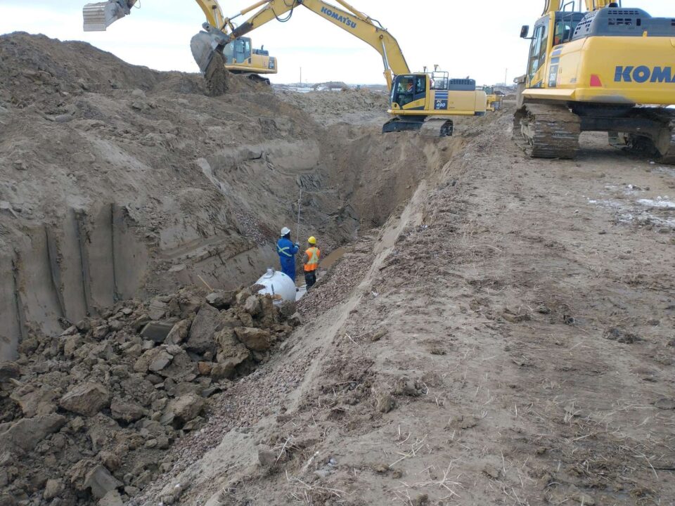Heavy equipment is used to install large white pipelines that will carry water for an irrigation network