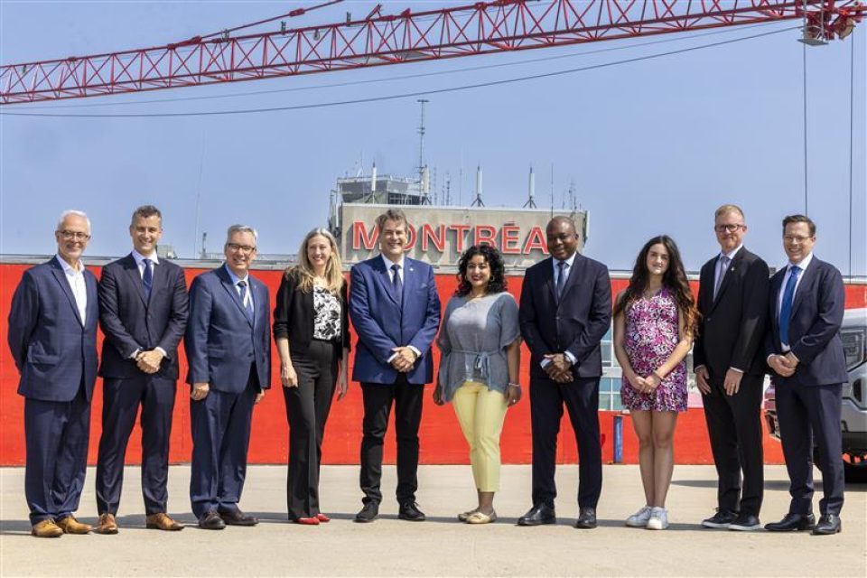 Des hommes et des femmes se tiennent devant un fond rouge et le logo de Montréal sous un ciel bleu.