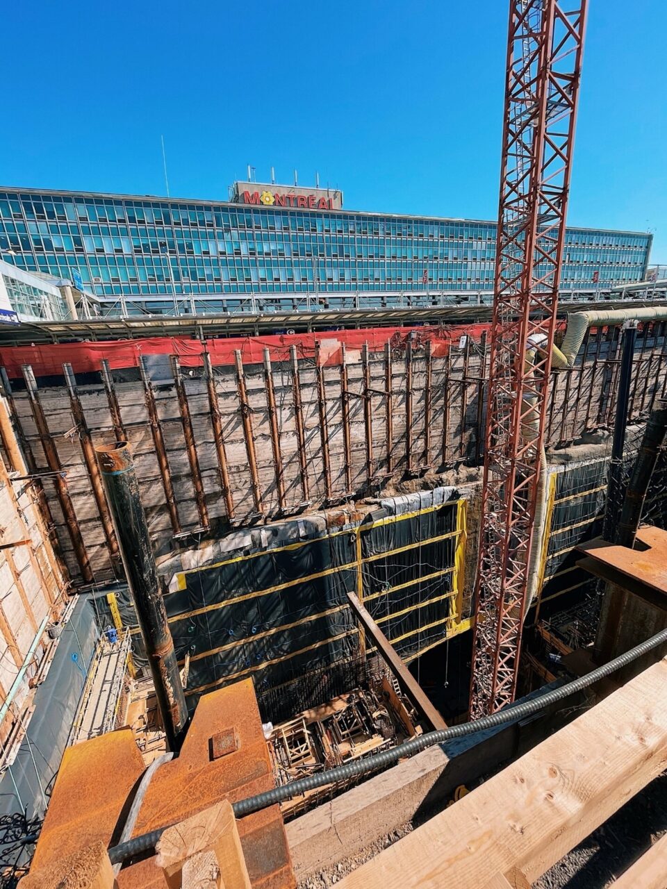 Large cranes enable work crews to operate in a deep open shaft to build the tunnel and station for the REM at Montreal’s Trudeau International Airport.