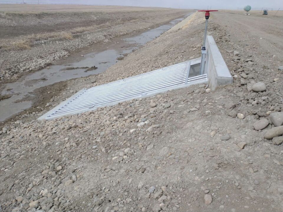 A large metal grate is visible along an irrigation network that will be used to water farmer fields